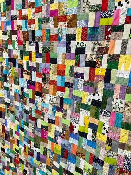 A close-up of a very dense, colorful scrappy quilt, showing the immense number of small fabric pieces used.