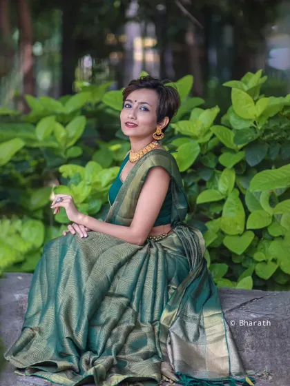 A serene and elegant outdoor portrait. The green of the saree complements the natural foliage perfectly.