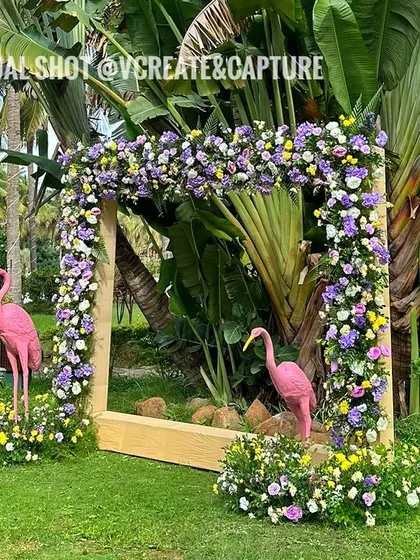 A flamingo-themed photo booth with a large floral frame, perfect for a tropical or poolside party.