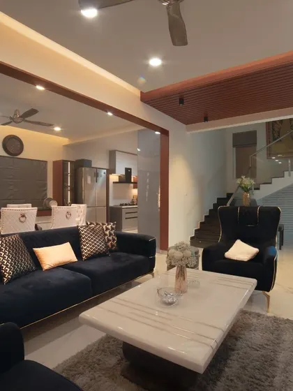 An open-plan living area from our project for Ms. Megha Joshi. The deep blue sofa with gold-accented cushions creates a striking focal point, while the marble coffee table adds a touch of luxury. The layout seamlessly connects to the dining and kitchen areas.