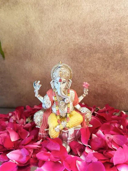 A beautifully hand-painted silver-plated Ganesha idol, surrounded by a bed of fresh rose petals. The soft colors and intricate details make it a truly special piece.