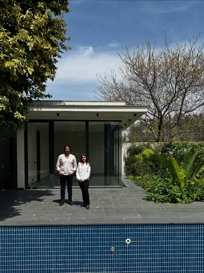 Our co-founders stand before the pool and guest house at the House of Passages. The clean lines of the pool and the minimalist architecture of the building create a serene and contemporary backyard setting.