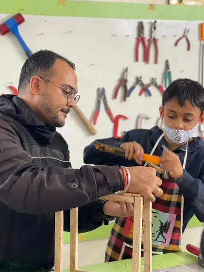 A father and son work together on a project, with the instructor guiding them on proper hammering techniques. Our workshops are great for family bonding.