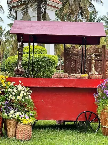 A vibrant red food cart surrounded by colorful flowers, part of a fun carnival-themed event.