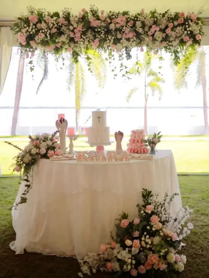 A beautiful cake table setup for a Baptism ceremony. The hanging floral arrangement and delicate pink and white flowers create a serene and elegant look.