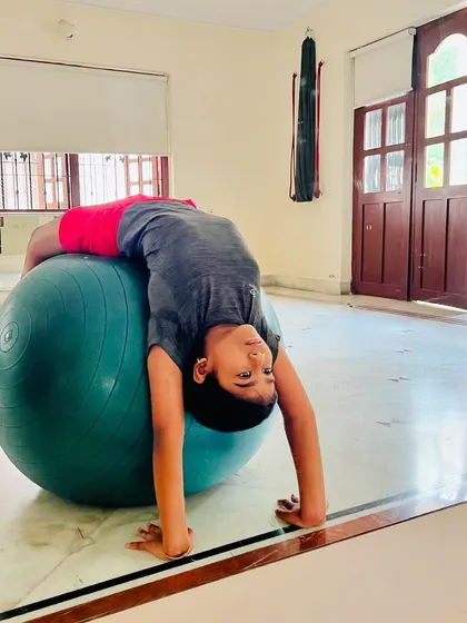 A young student uses a large stability ball to practice a backbend. This is a great tool for building back flexibility and core strength in a controlled manner.