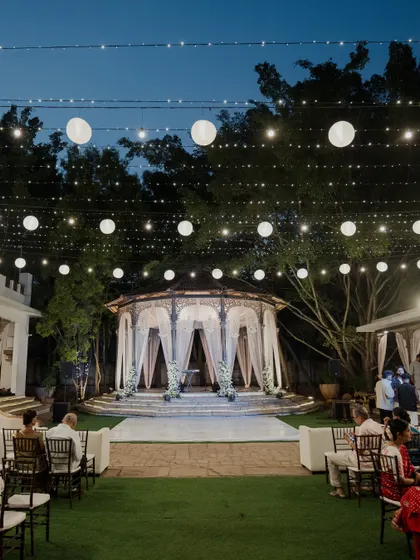 A dreamy pastel Sangeet setup under a canopy of paper lanterns and fairy lights. The soft lighting and elegant seating create a romantic and sophisticated atmosphere.