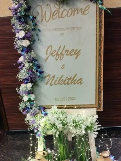 A modern welcome sign for a wedding reception, framed with a beautiful arrangement of purple and white flowers.