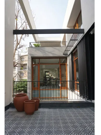 A view of the terrace with patterned cement tiles, terracotta pots, and a simple metal railing. The design focuses on the beauty of honest, simple materials.