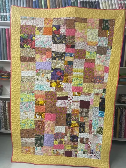 A scrappy quilt with a mix of many different fabrics and colors, bordered in a cheerful yellow.