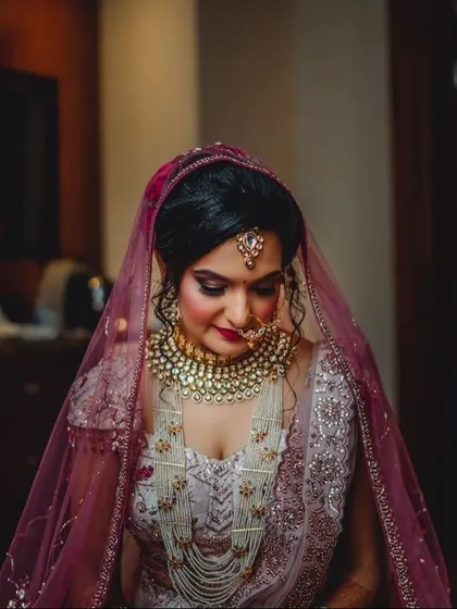 A bride looking down, showcasing her intricate pearl and kundan jewelry and the delicate embroidery of her lehenga.