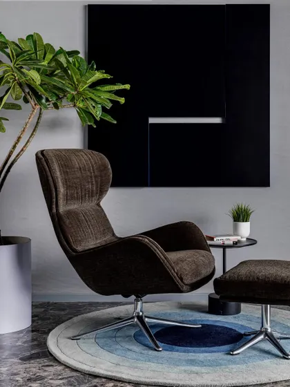 A comfortable reading corner featuring a modern swivel chair and ottoman, demonstrating how we create cozy nooks within larger open-plan spaces.
