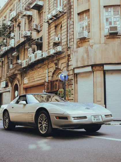 A sleek, silver Chevrolet Corvette, a classic American sports car, pictured on the streets of Mumbai. The low angle gives it a powerful and imposing presence.