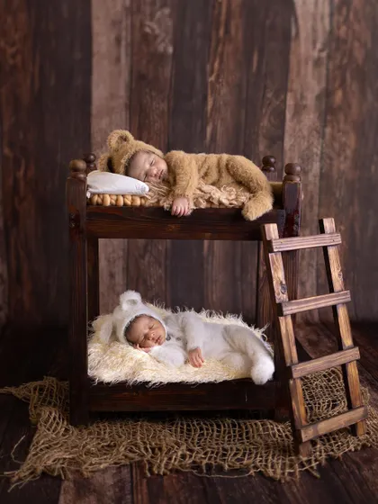 An artistic and heartwarming newborn portrait of twins, each sleeping peacefully in their own level of a miniature wooden bunk bed. This shot highlights our creative and safe approach to capturing your baby's first precious moments.