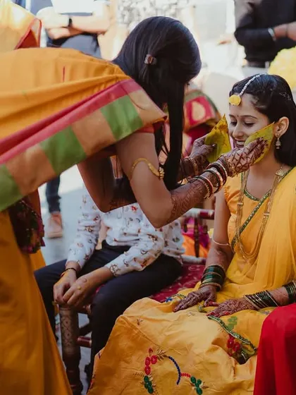 The bride receives blessings and Haldi from a family member, her expression calm and happy.