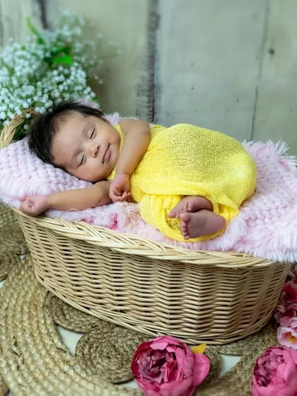 A little ray of sunshine. This newborn is sleeping so peacefully in a cozy basket, dressed in a bright yellow outfit that matches her sunny disposition.