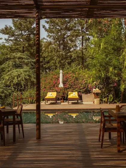 The view from the covered pavilion, looking out over the dining tables to the sun-drenched pool and loungers.
