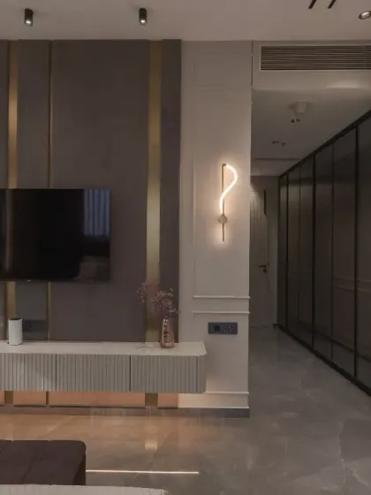 This bedroom space exudes modern elegance with its bespoke design. The fabric paneling, accentuated by gold trims, creates a rich backdrop for the floating console and sleek TV unit, optimizing vertical space.