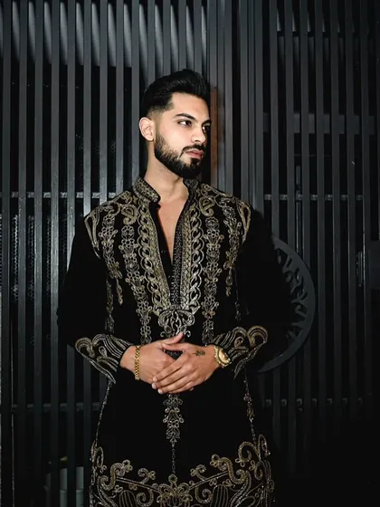 A three-quarter view of the black velvet kurta, showing how the intricate gold handwork extends down the front and along the cuffs, creating a cohesive and luxurious design.