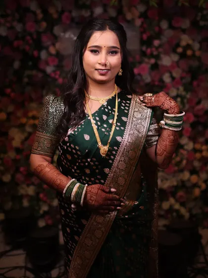 A beautiful portrait against a floral backdrop. The bride's makeup in her dark green saree is classic and elegant, with a focus on glowing skin.