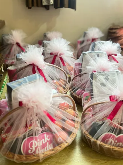 A large order of 'Pink Lady' themed gift baskets, all wrapped and ready for delivery. Each basket is consistently styled with pink tulle and ribbons to match the brand's color scheme.