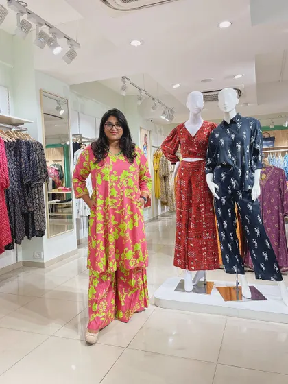 The stylist stands in a store wearing a vibrant pink and green floral co-ord set.