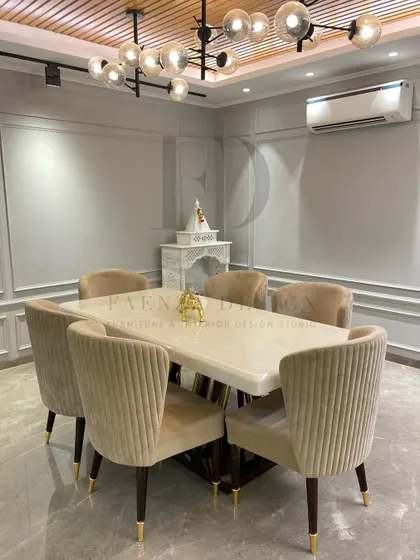 A serene and elegant dining space. The table, with its white onyx top and sculptural gold and wood base, is surrounded by plush, channel-tufted chairs in a soft beige velvet.