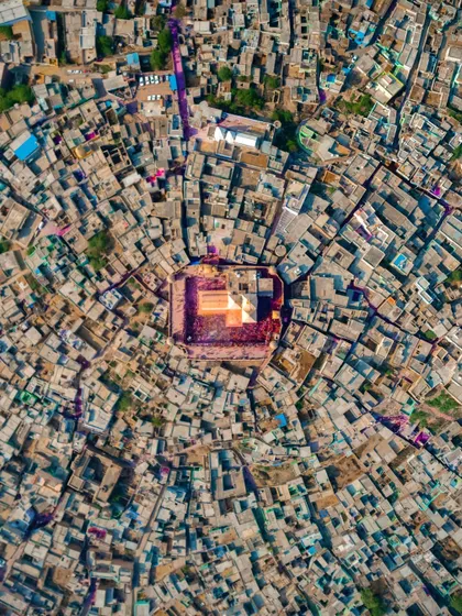 A top-down aerial photograph of the Holi celebration at Nandgaon temple, with the vibrant colors of the festival contained within the temple courtyard, creating a stunning contrast with the surrounding city.