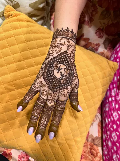 A single hand shot of the engagement mehendi, focusing on the intricate details surrounding the couple's initials.