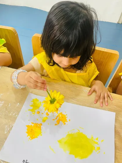 With great concentration, a young girl makes yellow imprints on her paper. This dip-and-dab activity is perfect for developing fine motor skills in our youngest learners.