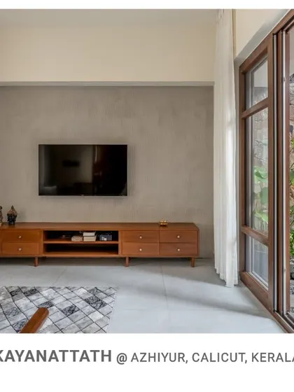 This view from the living room at Kayanattath House shows the seamless transition to the courtyard through large sliding glass doors, which feature a stone wall and a vibrant red jali screen.
