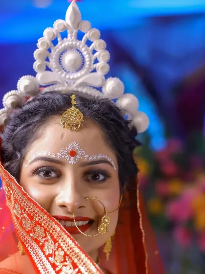 A peek-a-boo shot of a Bengali bride, her happy face framed by her red and gold saree.