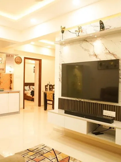 An open-concept living area where the TV unit, featuring a marble back panel and bronze mirror accents, serves as a stunning focal point. The design seamlessly connects the living space to the kitchen and dining areas.