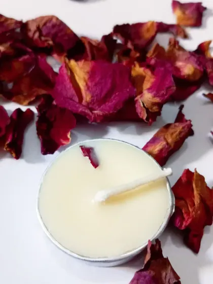 A close-up of a single tealight, showing how a delicate rose petal is embedded in the creamy soy wax.