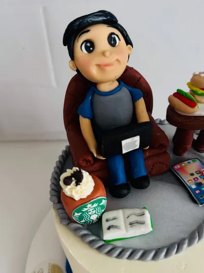 A close-up of the handcrafted fondant figure for a 50th birthday cake, showing him relaxing with his laptop.