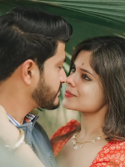 A close, intimate pre-wedding portrait framed by lush green leaves. This shot focuses on the couple's gaze, creating a feeling of being lost in their own world.