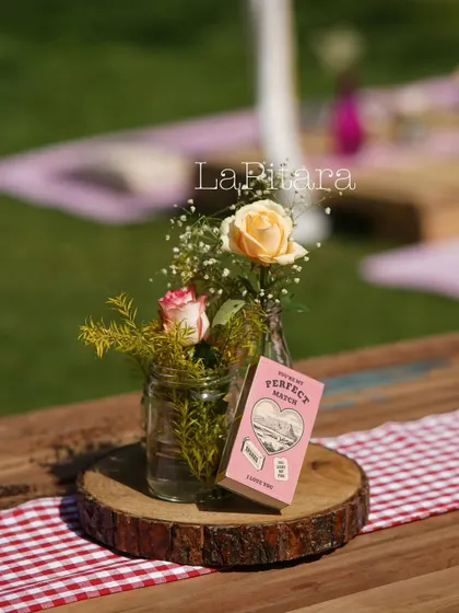 A charming detail from the Valentine's picnic. The table decor included simple floral arrangements in glass jars, set on a rustic wood slice, with a custom-designed "Perfect Match" matchbox as a playful accent.