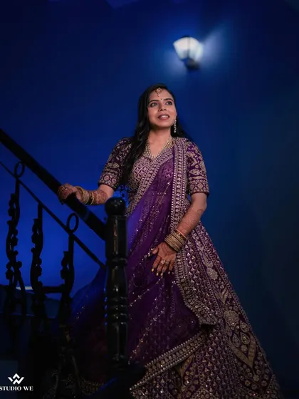 A portrait of the bride on a staircase, her purple lehenga creating a stunning visual against the blue-lit background.