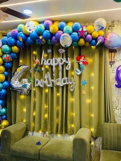 An under-the-sea mermaid theme for a 4th birthday, with a balloon arch in shades of blue, purple, and gold, plus mermaid tail and seashell foil balloons.