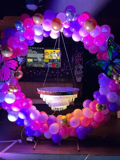A stunning chandelier cake stand hanging within a circular balloon frame. This unique butterfly-themed setup is perfect for making a statement at any birthday party.