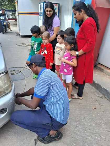 A group of K1 and K2 preschoolers watch a petrol pump attendant check a car's tire during their field trip.