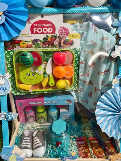 A finished first birthday hamper for a boy, decorated with blue balloons and filled with toys and clothes.