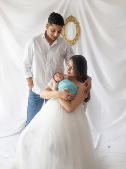 A classic family portrait with their newborn. The mother's flowing white dress and the baby's peaceful sleep create a beautiful and elegant scene.