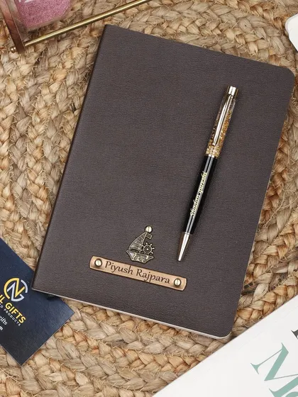 A personalized brown leather diary with a ship charm, paired with a matching gold flake pen. The diary is shown on a rustic jute mat.