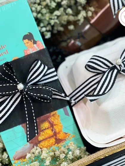 A close-up of the gourmet treats inside the groom-to-be hamper, tied with a classic black and white striped ribbon with a pearl accent.