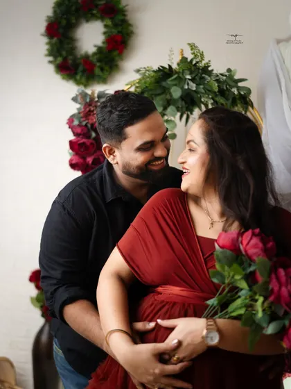 A happy, candid moment between the expecting couple. Their joyful interaction is the focus of this shot, surrounded by a beautiful red floral arrangement.