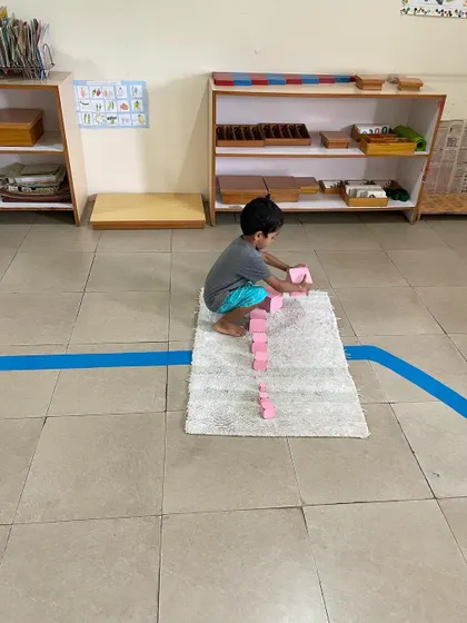 A child works with the Pink Tower, a classic sensorial material. This activity helps them visually discriminate between sizes and builds their understanding of dimensions, which is an indirect preparation for mathematics.