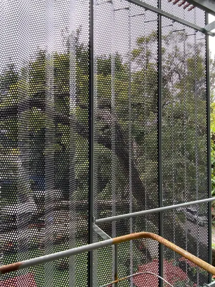 A view through the perforated metal screen we designed for a commercial building in Bangalore. The folded, layered skin acts as a veil, reducing glare and creating a dynamic play of light and shadow while offering a modern counterpoint to the surrounding greenery.