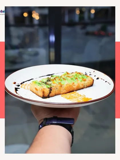 A hand holds up a plate of our cheesy garlic bread. It's a classic comfort food, elevated with high-quality cheese and a perfect garlic flavor, then drizzled with balsamic for a gourmet touch.