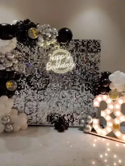 This glamorous setup for a 38th birthday features a full silver sequin shimmer wall. It's complemented by a balloon garland, a circular neon sign, and large marquee numbers, creating a truly high-end party look.